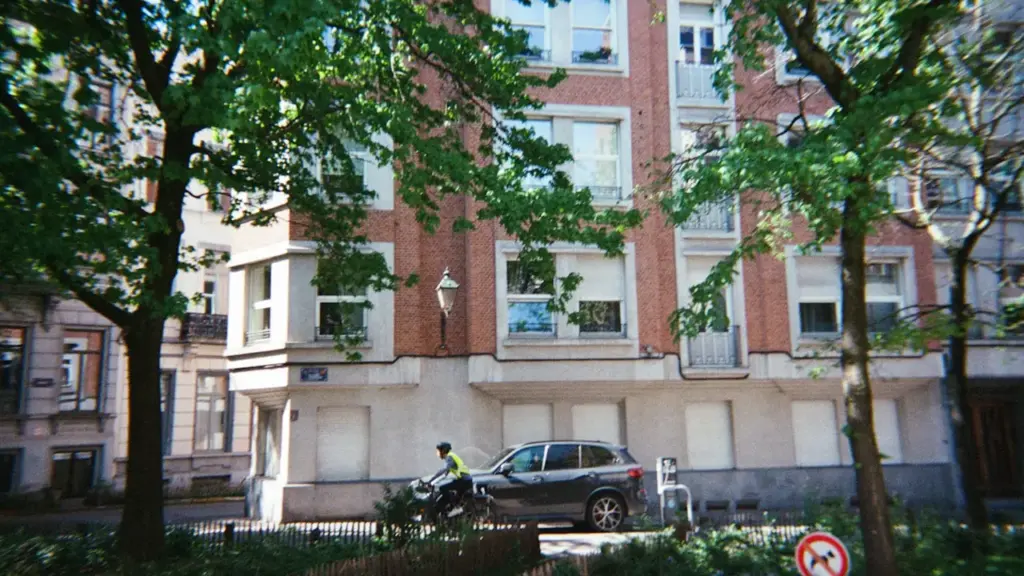 A cyclist rides past a brick apartment building on a tree-lined city street.